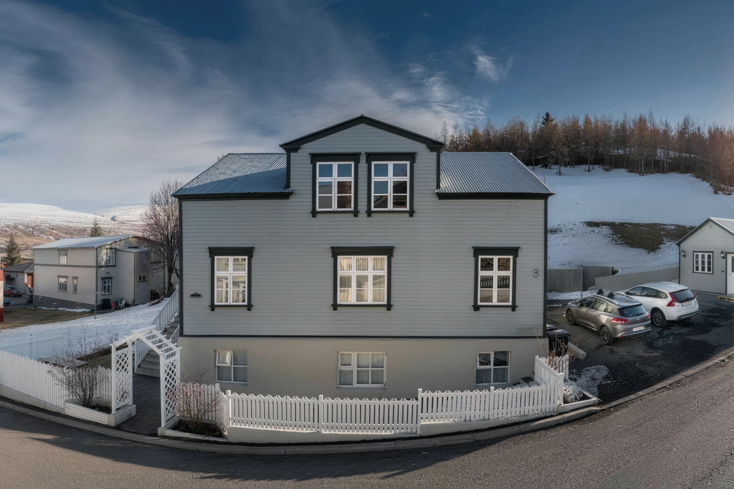 Akureyri Lodge, the pale green timber house at Lækjargata 3 seen from the street corner, white fence in front, hillside behind