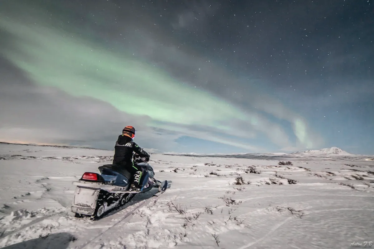 A snowmobile rider crossing open snow beneath the northern lights